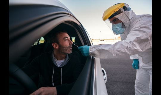 Lab tech in protective gear checks patient in car