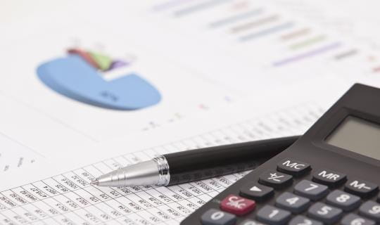 Calculator beside a pen and financial analysis paper
